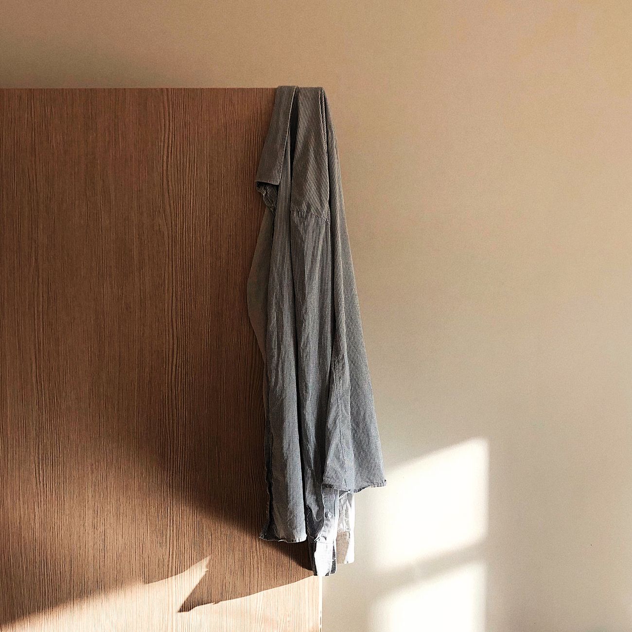 A simple shirt hanging on a wooden door with warm sunlight streaming in, creating a minimalist aesthetic.